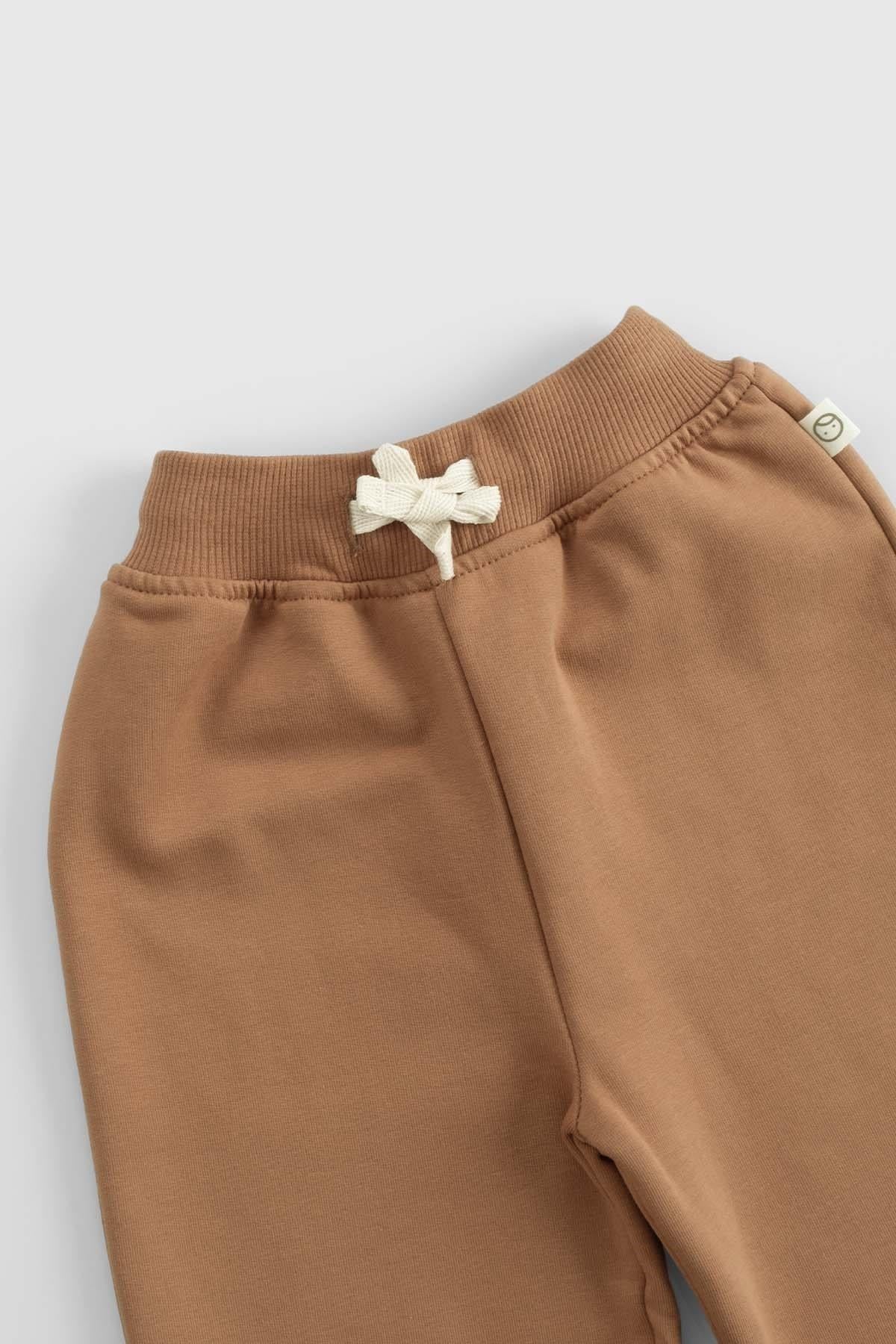 Close-up of brown organic cotton baby tracksuit pants with ribbed waistband and bow detail.