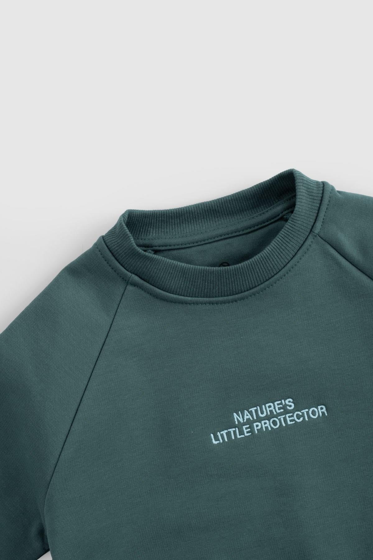 Close-up of organic cotton baby tracksuit top featuring 'Nature's Little Protector' embroidery in green.