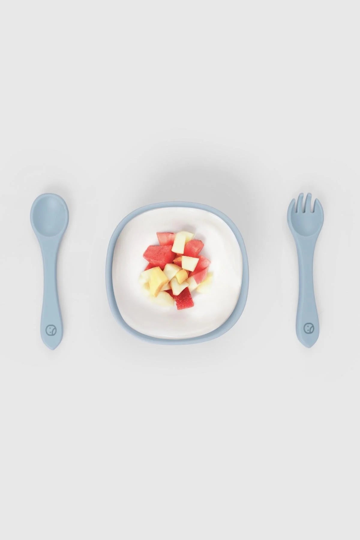 Silicone vacuum food plate with cutlery set in blue, containing diced watermelon and apple pieces for toddlers.