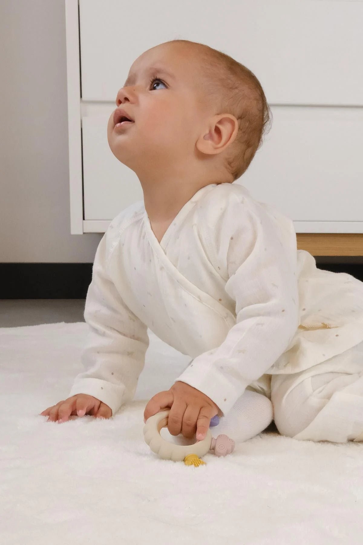 Baby playing with Little Gusto silicone and wooden teether, promoting sensory exploration and grasping skills.